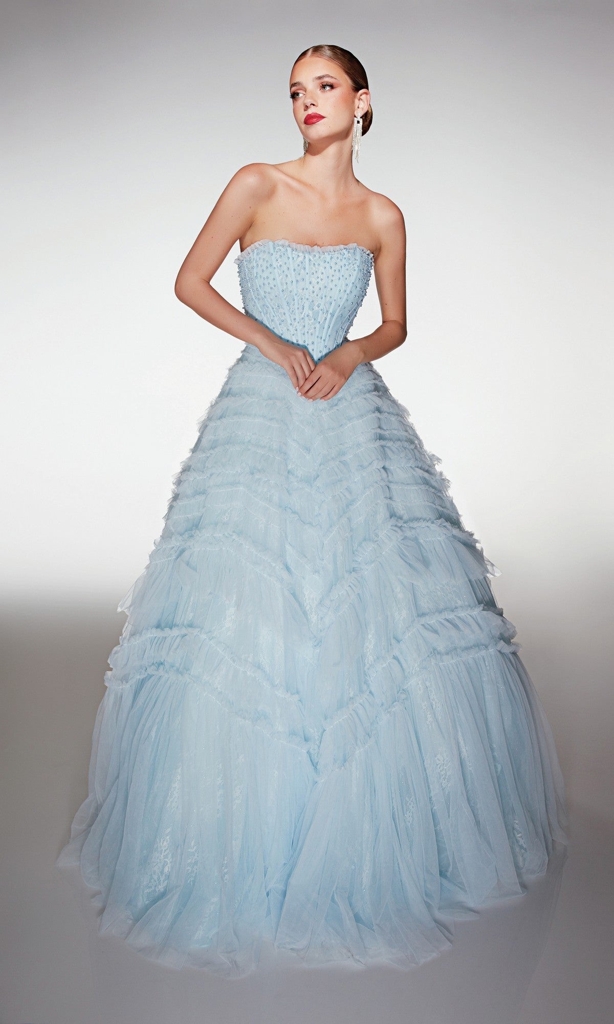 A woman poses gracefully in the Alyce 62208 long prom dress, featuring a strapless beaded bodice and a full layered tulle ruffle skirt, set against a plain background.